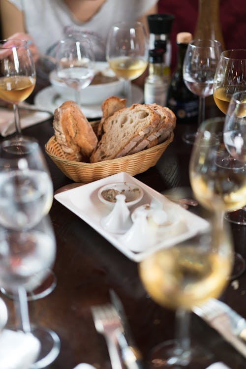 Free Oval wicker bowl of delicious fresh bread and glasses of wine on table in restaurant with crop faceless people dining out Stock Photo
