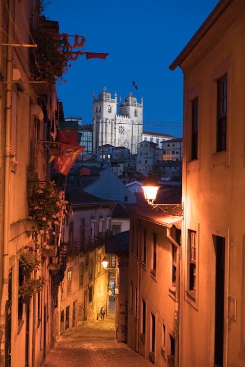 Free Narrow cobblestone street of Porto City lit with lanterns at dusk with Porto Cathedral on hill in distance Stock Photo
