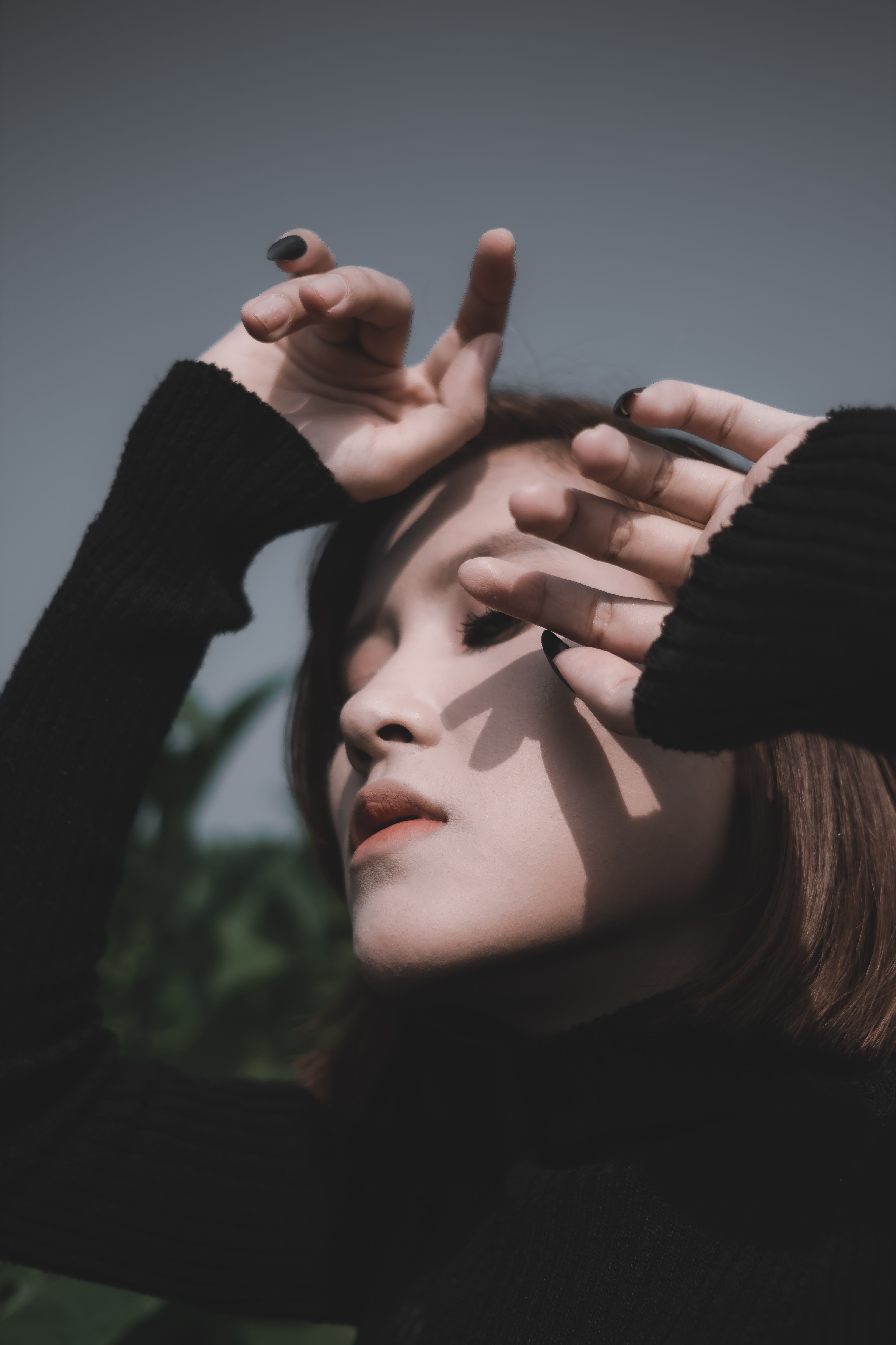 Tranquil serene female in black turtleneck standing with eyes closed in park and holding hands near face