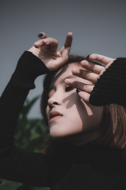 Tranquil serene female in black turtleneck standing with eyes closed in park and holding hands near face