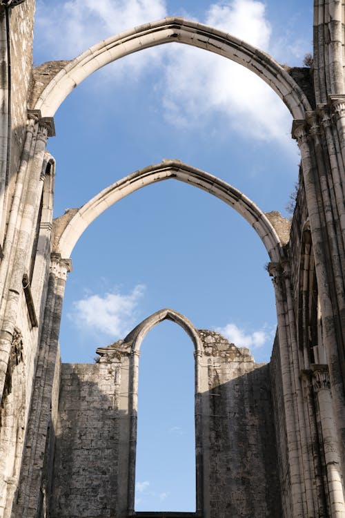 Free From below of ancient pointed stone arches of Convent of Lady of Mount Carmel in Portugal in sunlight under clear blue sky Stock Photo