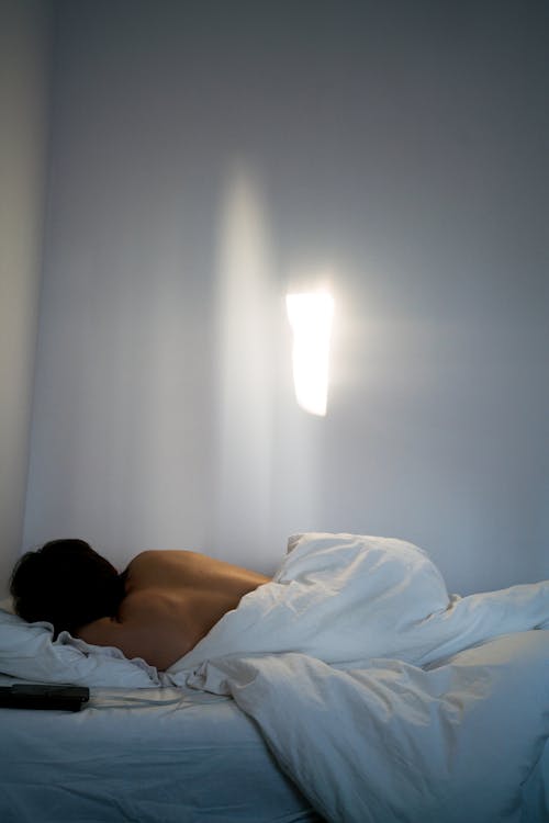 Free Unrecognizable person with bare back sleeping in bed Stock Photo