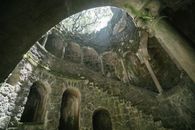 From below of dark moss grown Initiation Well with spiral staircase at Regaleira estate in Portugal
