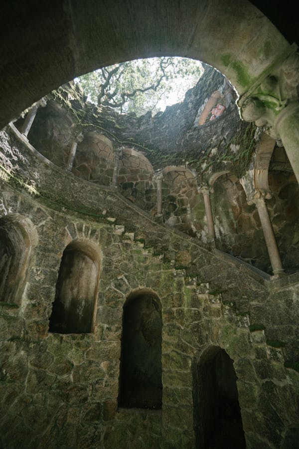From below of dimly lit Initiation Well with spiral stairway and walls grown with moss at Quinta da Regaleira in Portugal