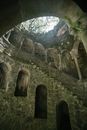 From below of dimly lit Initiation Well with spiral stairway and walls grown with moss at Quinta da Regaleira in Portugal
