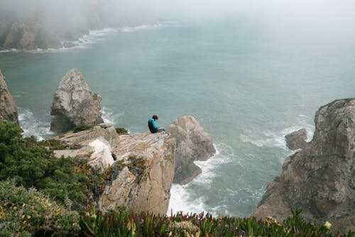 Unrecognizable man sitting on cliff above sea