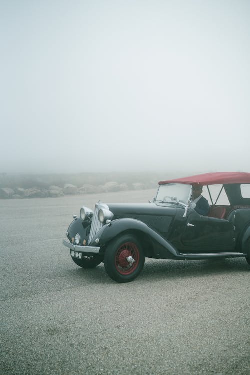 Unrecognizable man driving on retro fashioned car through fog on empty asphalt road