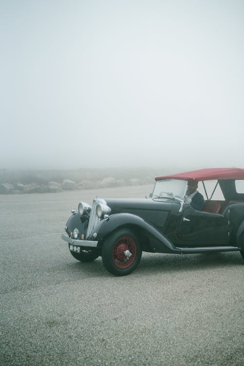 Unrecognizable man driving on retro fashioned car through fog on empty asphalt road