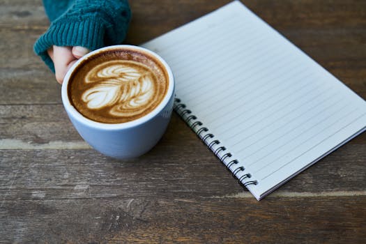 A serene setup of a latte with latte art and a notebook on a wooden table, ideal for a relaxed work session.