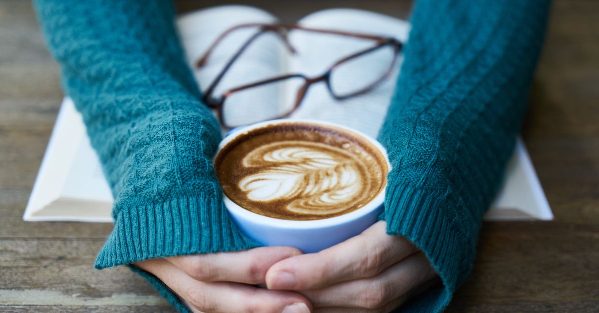 Hands warming over a latte art coffee, with book and glasses, creating a cozy indoor ambiance. - Evidence evidence guide for caffeine mental performance meta-analysis