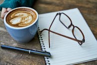 这个舒适的工作空间配备了拿铁艺术品、笔记本和眼镜，非常适合创意思考