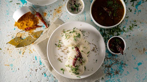 Free Top view of delicious Idli rice cakes with herbs and spicy tomato soup served on table near sauces and scattered spices Stock Photo