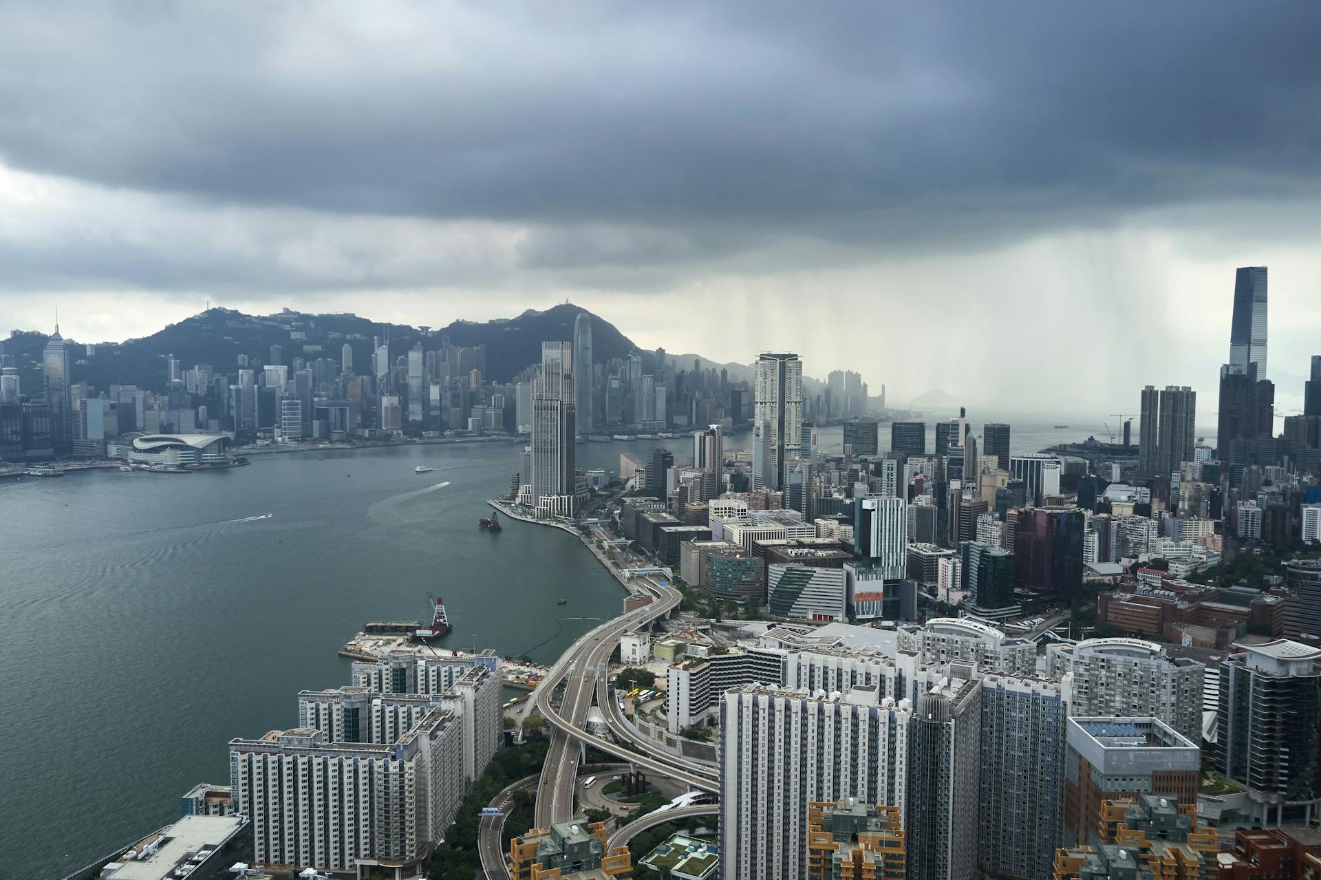 A breathtaking aerial view of Hong Kong's Kowloon skyline under dark, stormy clouds.