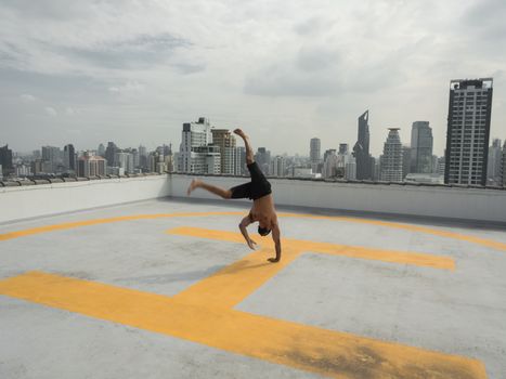 Man performing a cartwheel on a rooftop helipad with a city skyline backdrop.