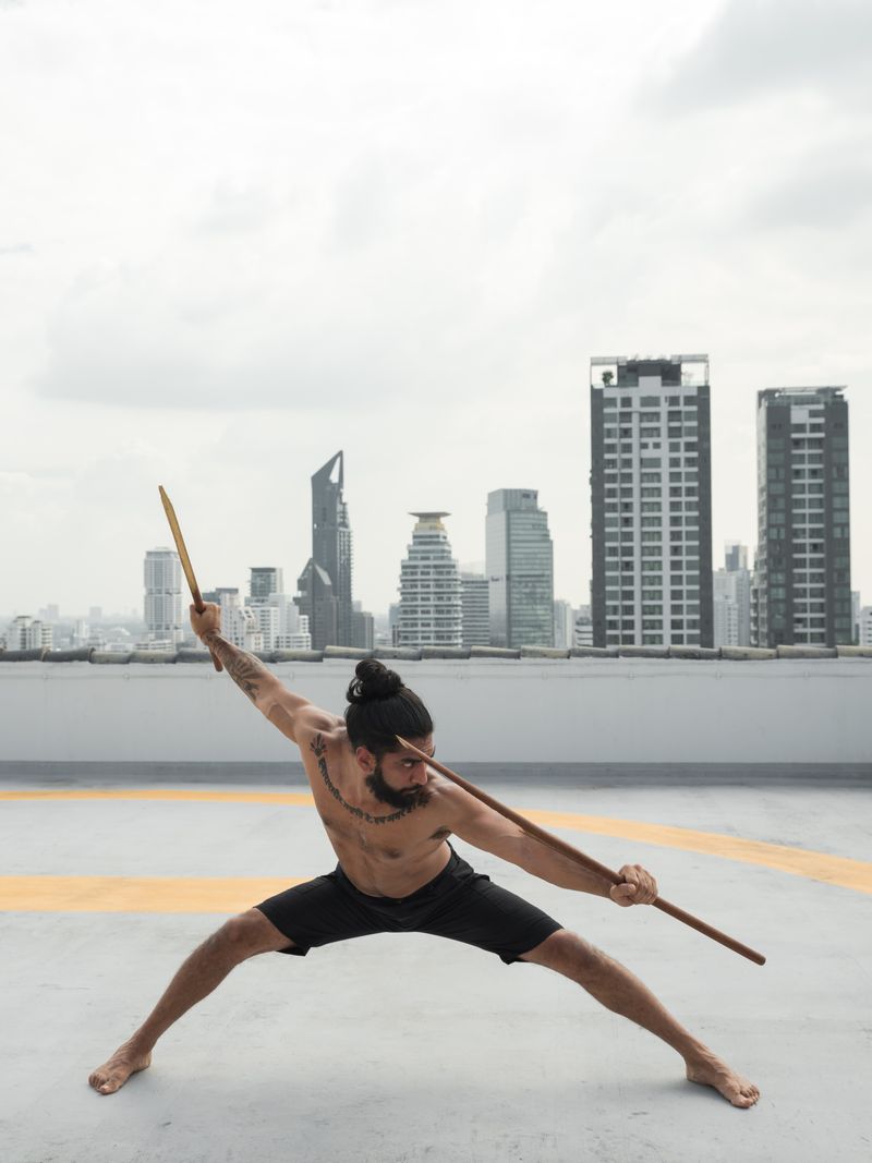 Eskrima practitioner training with sticks against a city skyline