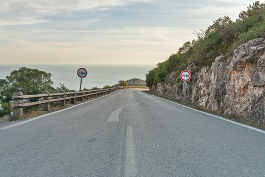 Empty road with scenic ocean view in Setúbal, Portugal, flanked by road signs and rocky cliffs.