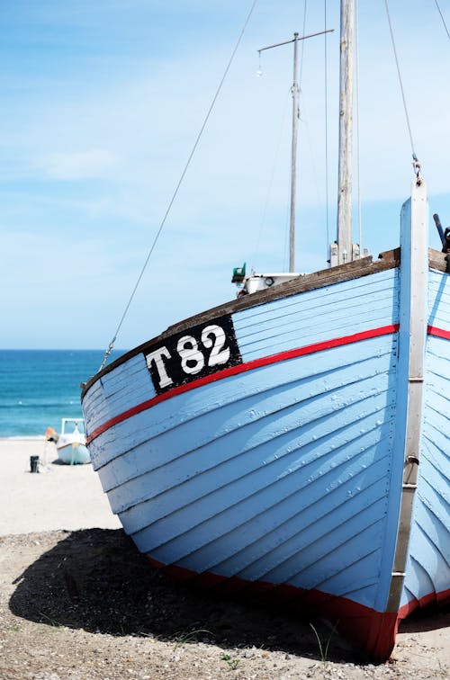 Blue vessel with number located on sandy shore near sea water against cloudy sky on sunny day