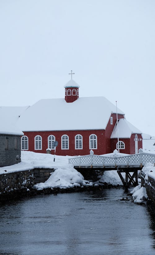 Church building covered with snow located on shore of cold river near bridge in winter