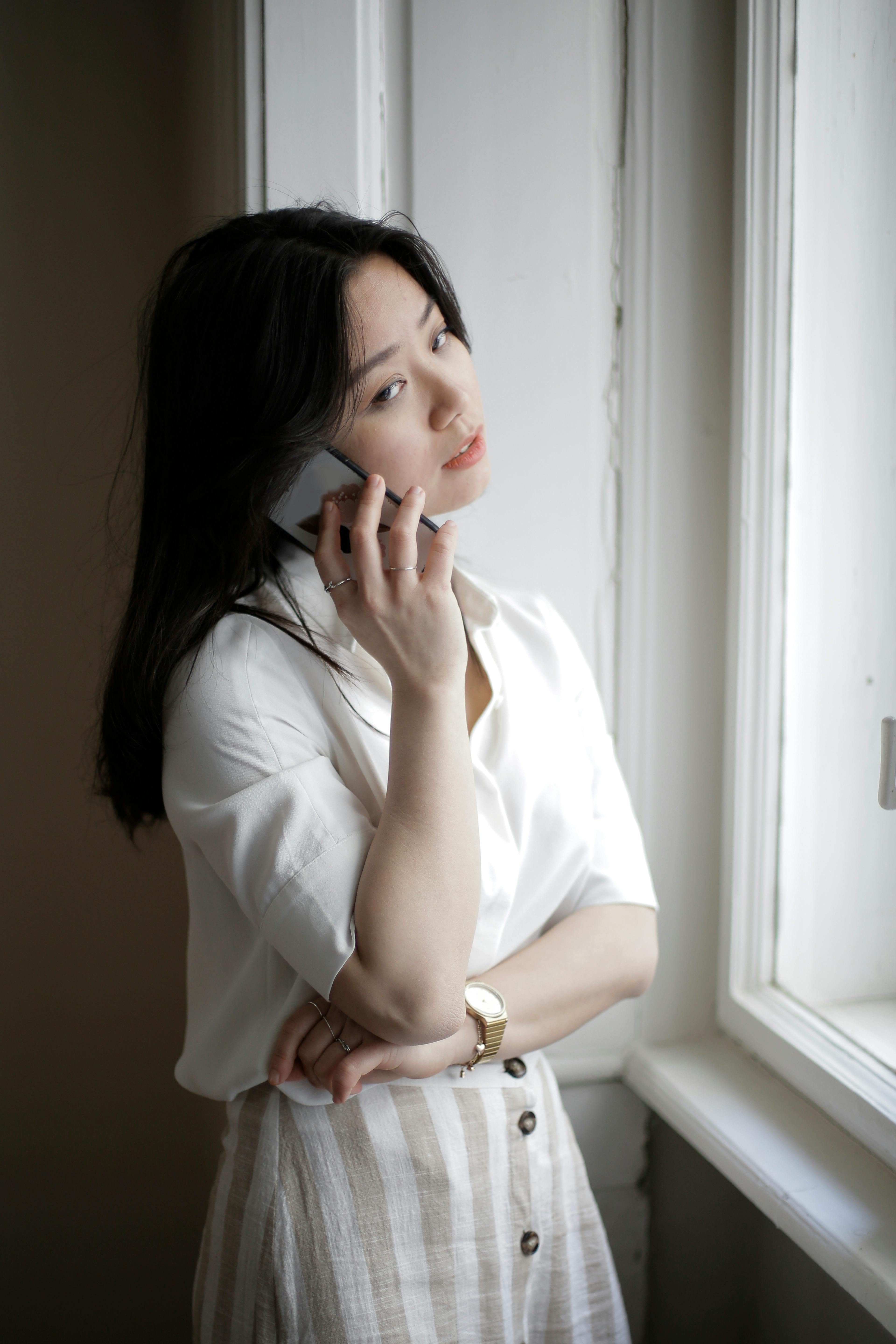 young asian woman speaking on smartphone near window