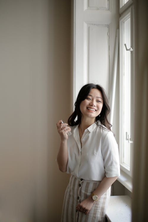 Gratuit Femme Asiatique Joyeuse Appliquant Le Parfum Près De La Fenêtre Photos