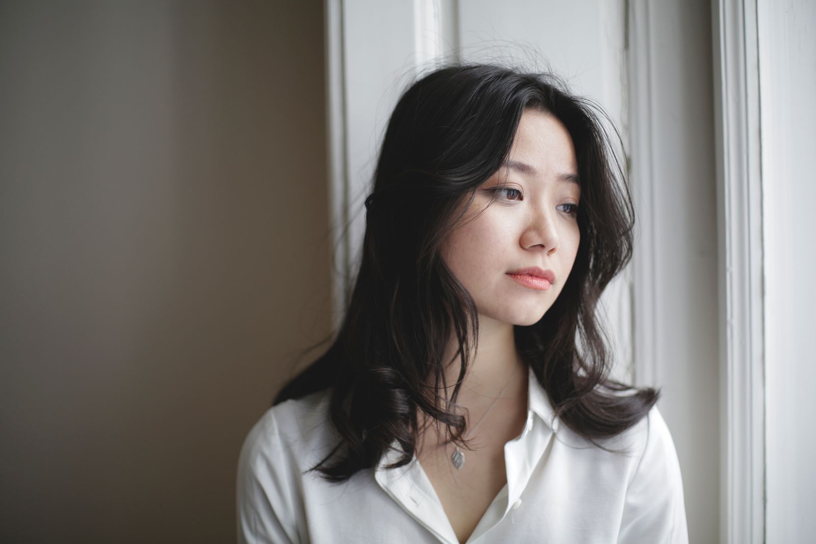 Reflective Asian adult by a window representing the hidden effort of autistic masking