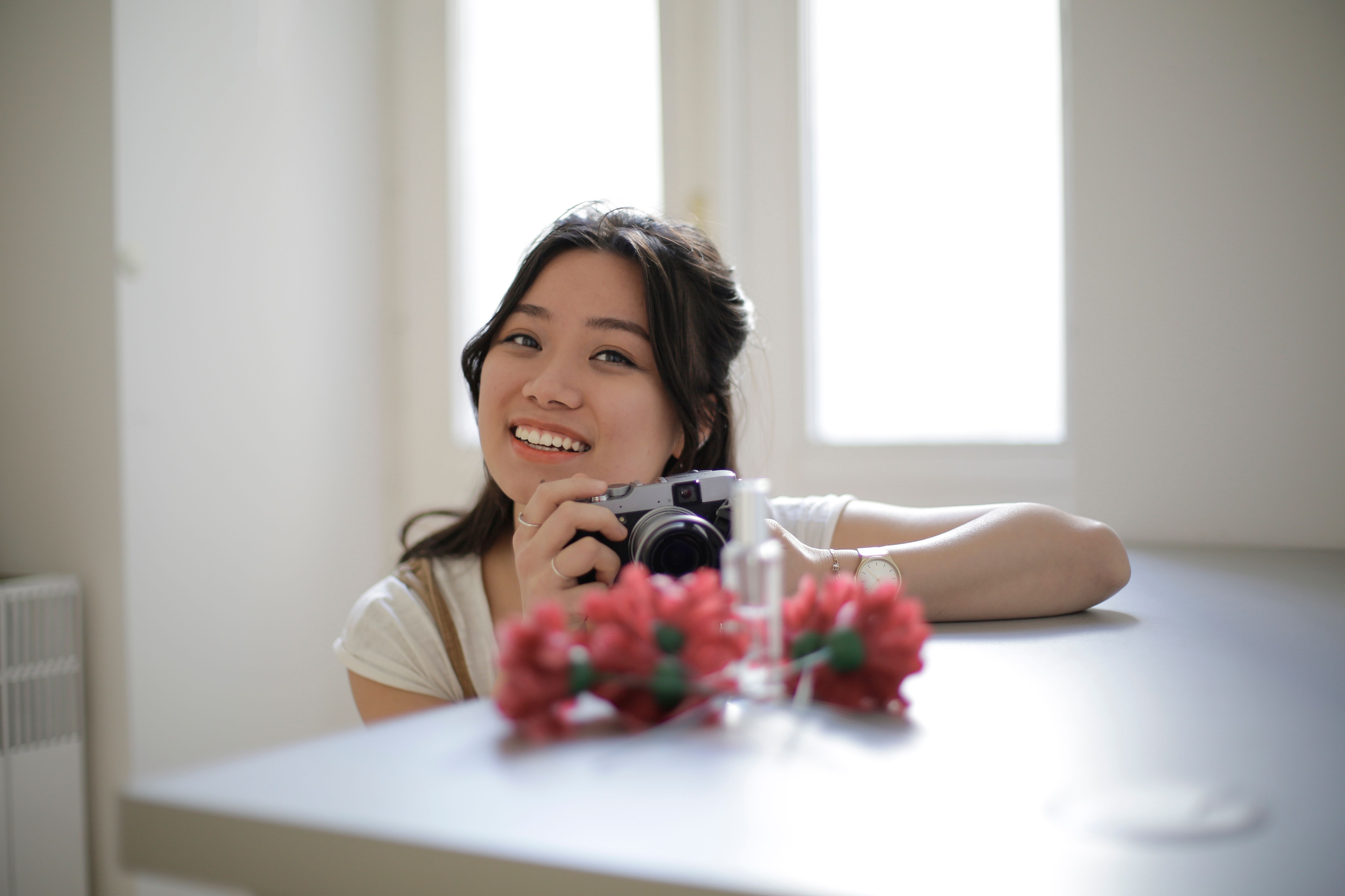 一个女人在室内拿着一台相机，旁边有一束鲜花