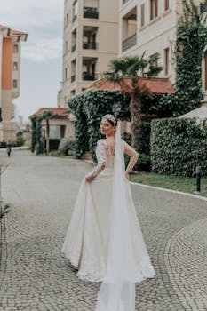 一位美丽的新娘身穿白色长袍、头戴面纱，微笑着站在阿塞拜疆的鹅卵石街道上