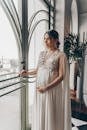 Young pregnant woman in vintage gown looking at window