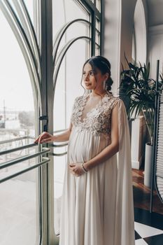 一位身着优雅礼服的孕妇宁静地望着窗外，展现出冷静与女性气质