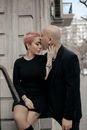 Stylish adult bald man kissing elegant sensual woman on forehead while having romantic moment near old gray building on city street