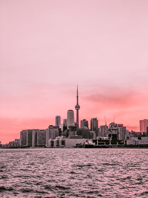 Amazing skyline of coastal city with contemporary buildings and high tower seen over rippling water against pink cloudy sunset sky