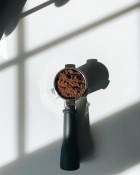 A portafilter with ground coffee casting shadows in bright sunlight.