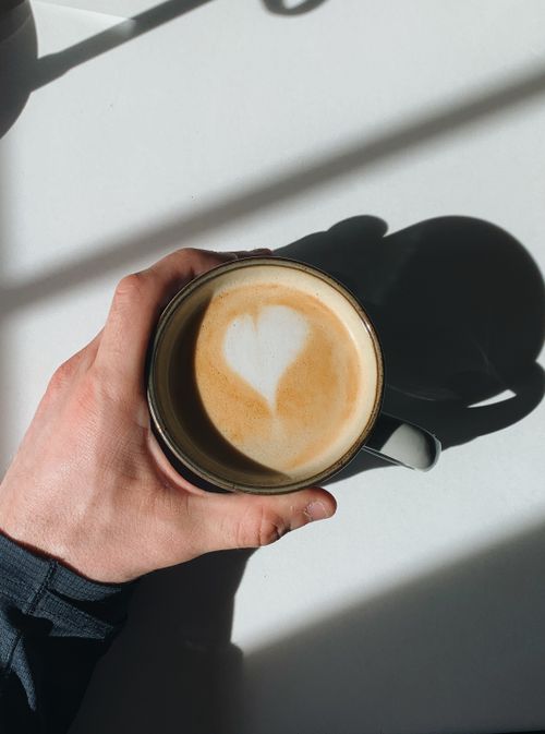 Free Aerial view of a hand holding a latte with heart-shaped art, casting shadows. Stock Photo
