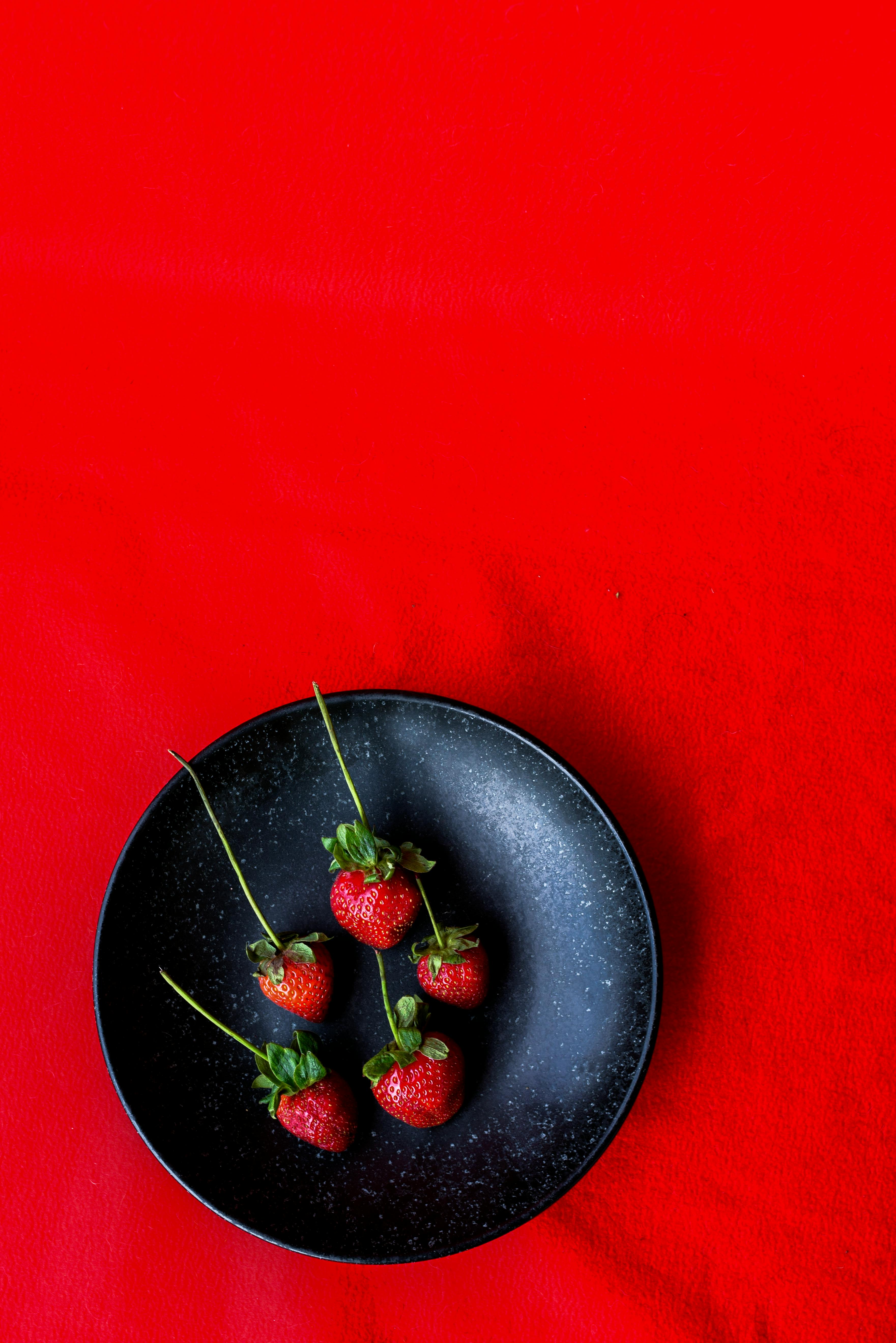 Top view of ripe strawberries on a black plate against a vibrant red background, perfect for food photography.