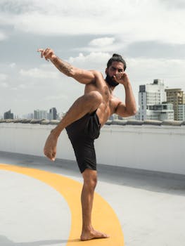 Shirtless man performs martial arts pose on a city rooftop, showcasing strength and balance.