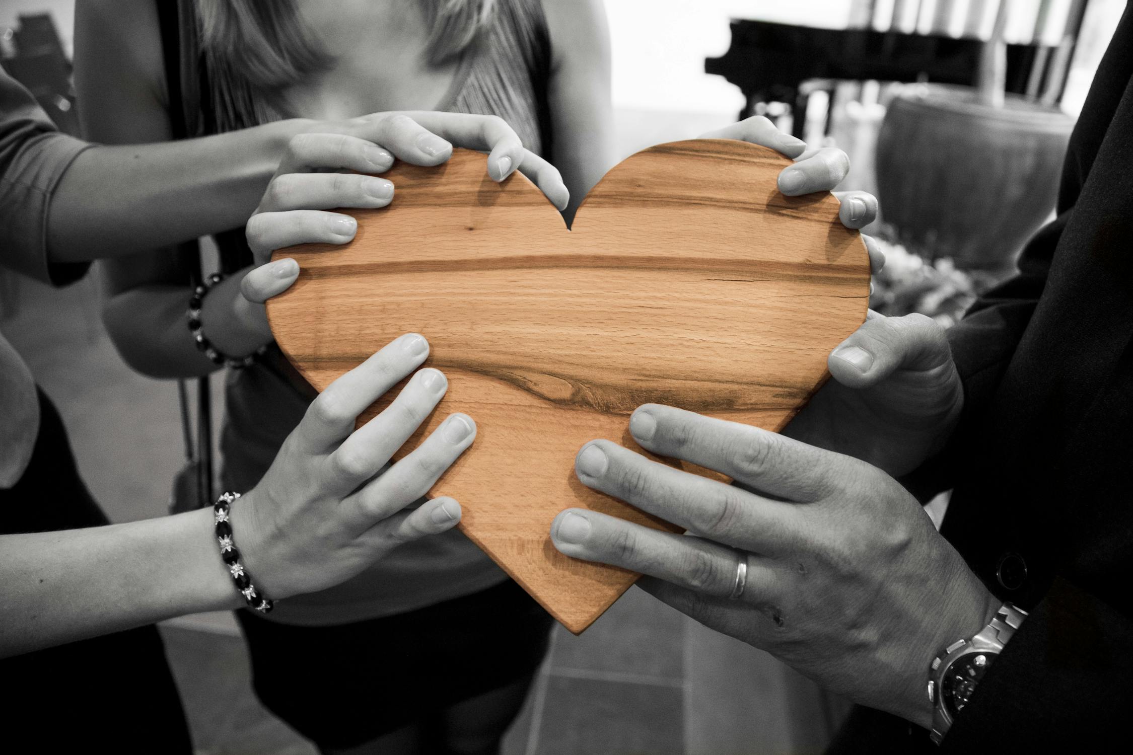 peoples hands holding a wooden heart