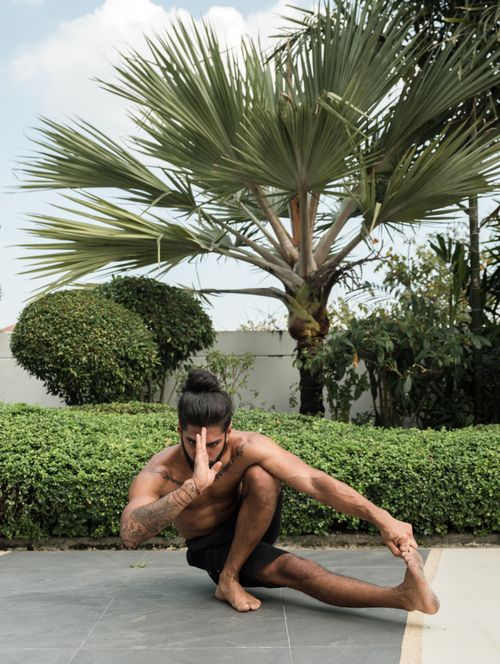 Free A shirtless man performing a yoga pose outdoors in a lush garden setting. Stock Photo