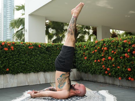 A tattooed man performing a yoga shoulder stand outdoors, showcasing strength and flexibility.