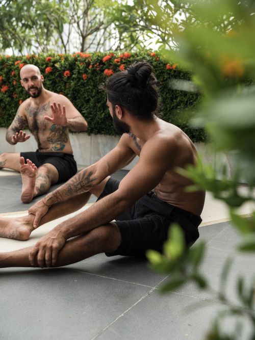 Free Tattooed men in black shorts sit and stretch, engaging in casual conversation outdoors. Stock Photo