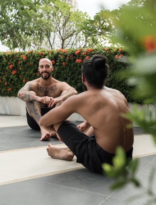 Free Full body shirtless bearded tattooed smiling males sitting on paved ground in garden and chatting on sunny day Stock Photo