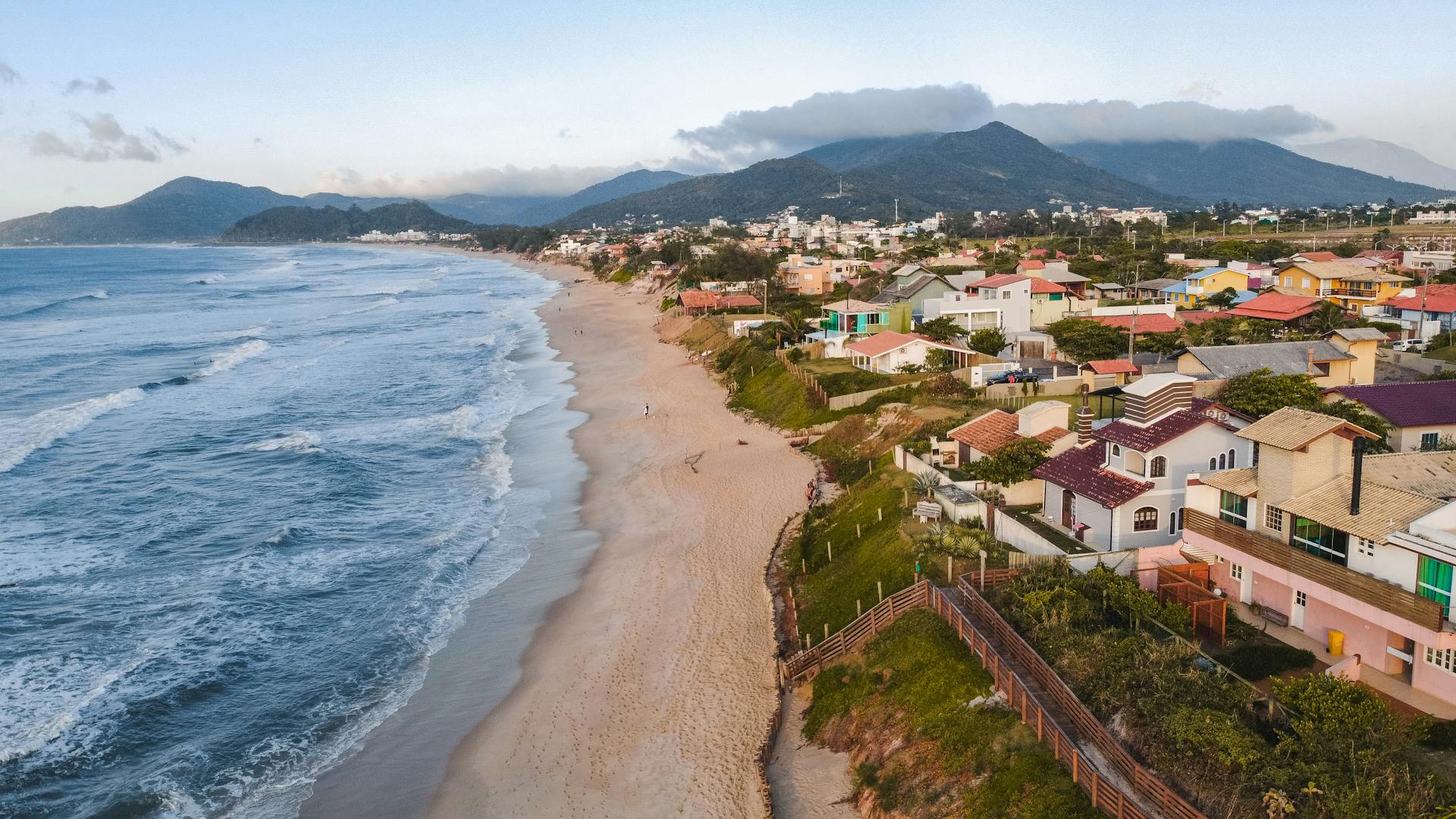 Aerial shot of a scenic beach in Santa Catarina, Brazil with houses and mountains in the distance.