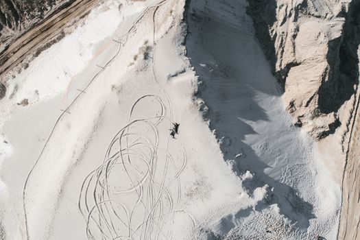 Drone view anonymous distant persons lying on white sand with curvy foot tracks on highlands during daytime