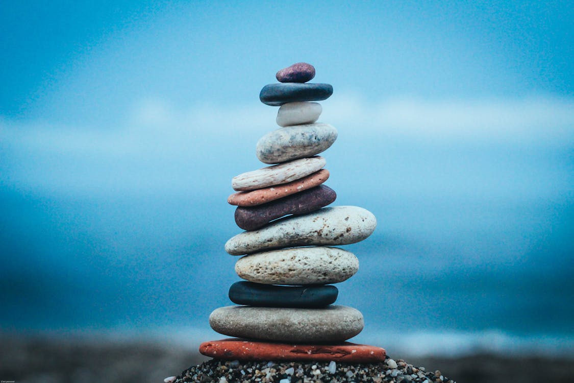 Closeup of stacked flat stones of various sizes and colors arranged on beach against blurred blue waving sea