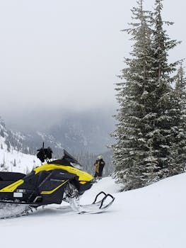 A person standing in a snowy mountain landscape with a snowmobile, capturing the essence of winter adventure.