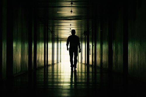 Free Shadowy silhouette of a person walking through a dark, dramatic hallway. Stock Photo
