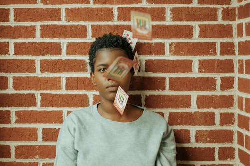 Cards Falling Around Young Woman Standing Against a Brick Wall