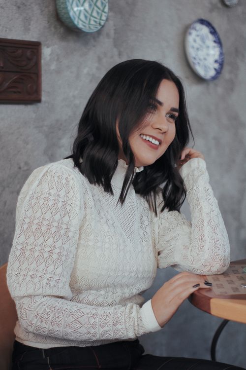 Free A cheerful woman with dark hair and white sweater enjoying her time in a cozy cafe with decorated walls. Stock Photo