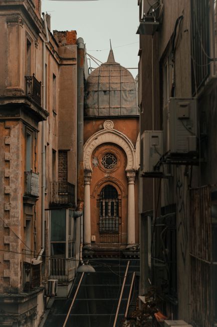 Aged stone building with dome and ornamental arched decor located against weathered houses on narrow street of old city district