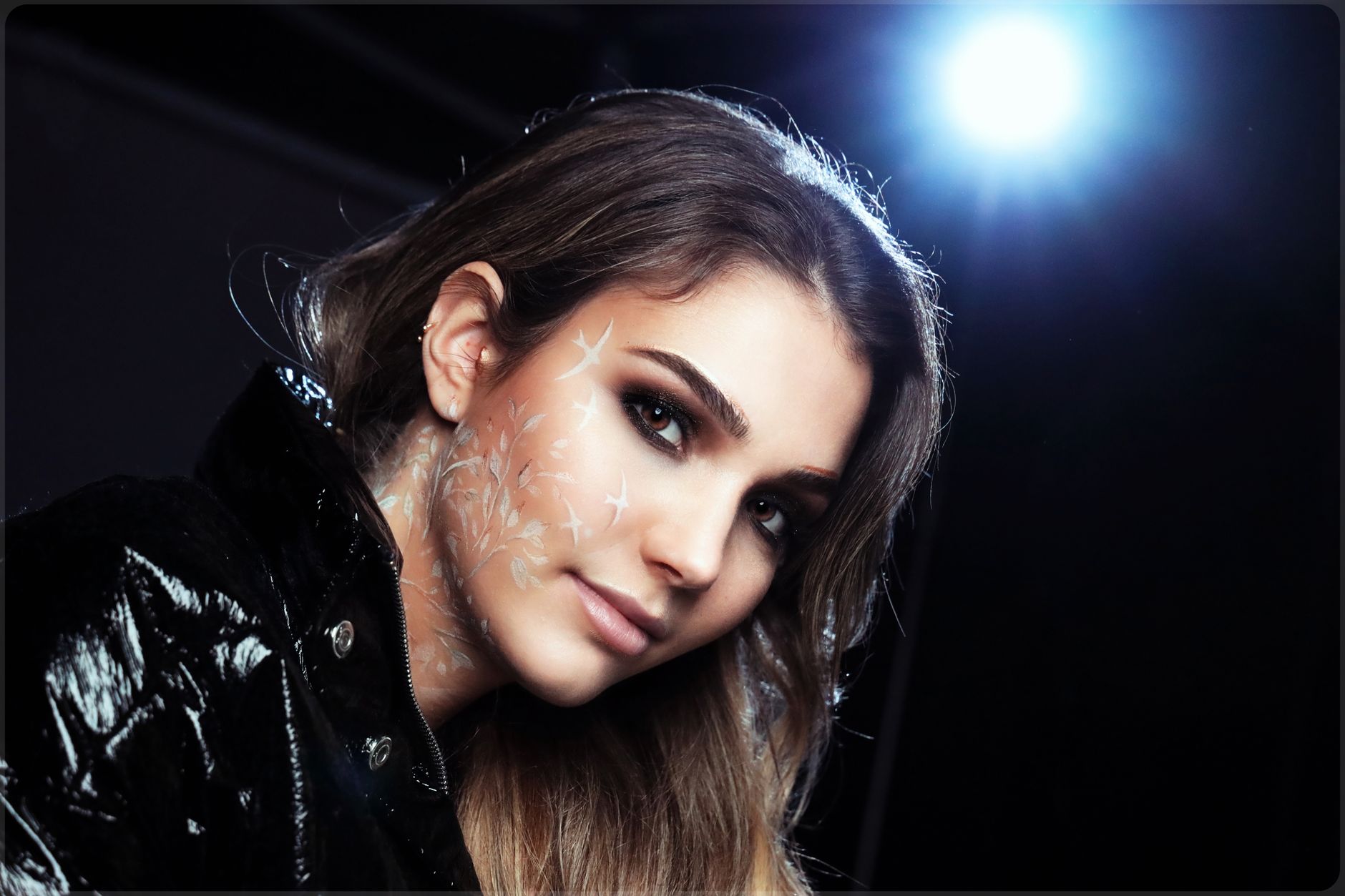 Close-up of a woman with creative face paint and artistic makeup in a studio setting.