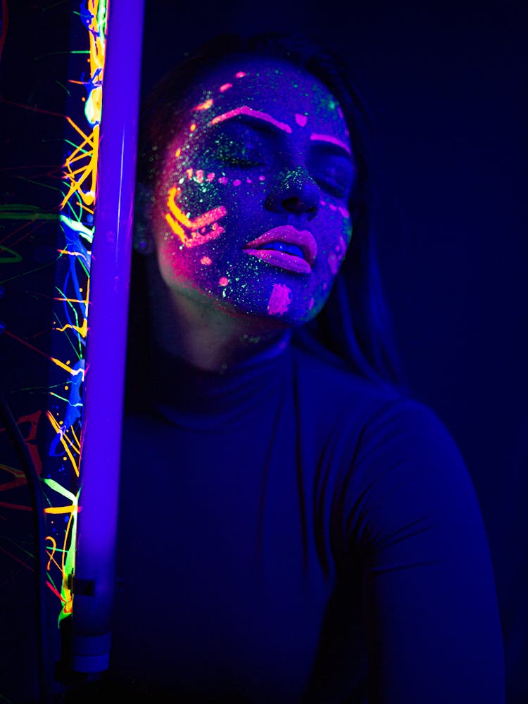 Calm Woman With Neon Paints On Face And UV Lamp